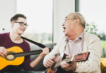 Senior man singing and playing guitar with his grandson - UUF006634