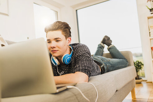 Junger Mann auf der Couch liegend mit Laptop - UUF006640