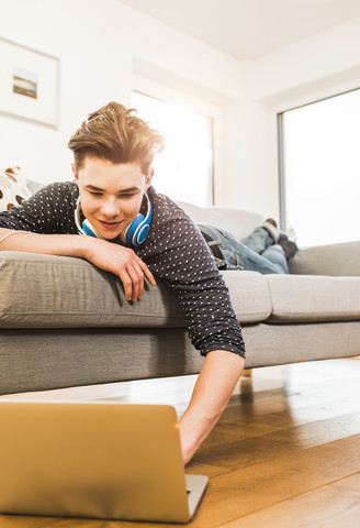 Young man lying on couch using laptop stock photo