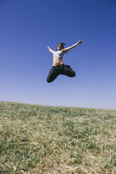 Glückliche Frau springt auf einer Wiese vor blauem Himmel - ABZF000195