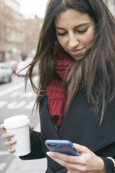 Spanien, junge Frau mit Kaffee zum Mitnehmen, die auf ihr Smartphone schaut - ABZF000198