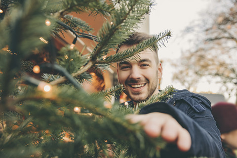 Glücklicher junger Mann mit einem Baum auf dem Weihnachtsmarkt, lizenzfreies Stockfoto