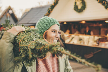 Happy woman with a wrapped-up tree walking over the Christmas Market - MFF002648