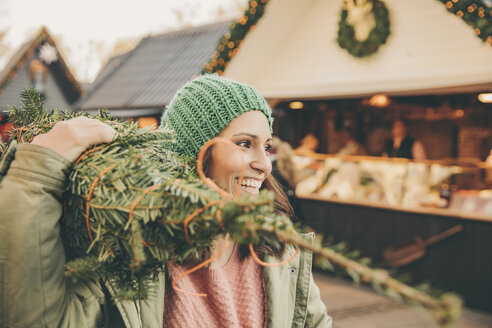 Happy woman with a wrapped-up tree walking over the Christmas Market - MFF002648