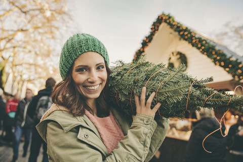 Glückliche Frau mit einem eingepackten Baum, die über den Weihnachtsmarkt läuft, lizenzfreies Stockfoto
