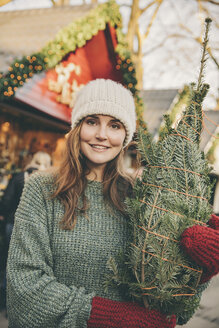Smiling woman with a wrapped-up tree standing on the Christmas Market - MFF002655