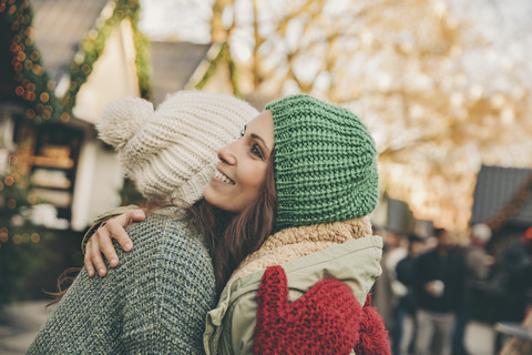 Glückliche Frauen beim Umarmen auf dem Weihnachtsmarkt, lizenzfreies Stockfoto