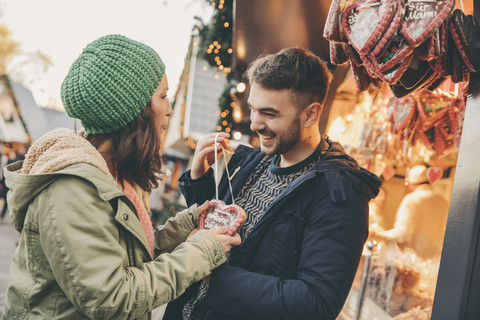 Frau erhält von ihrem Freund auf dem Weihnachtsmarkt ein Lebkuchenherz, lizenzfreies Stockfoto