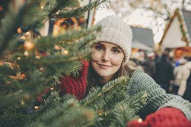 Frau schaut auf dem Weihnachtsmarkt durch Nadelbaumzweige - MFF002671