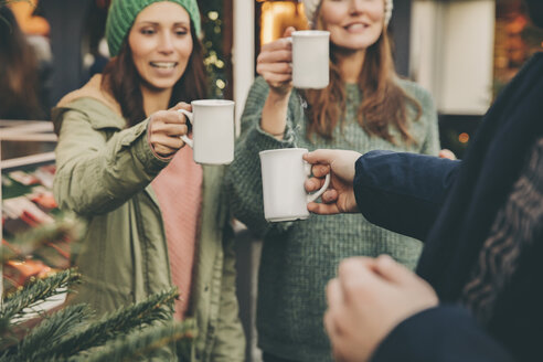 Fröhliche Freunde stoßen auf dem Weihnachtsmarkt mit einem Becher heißen Punsch an - MFF002679