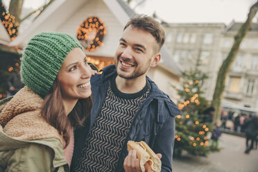 Glückliches Paar bei einem Imbiss auf dem Weihnachtsmarkt - MFF002682
