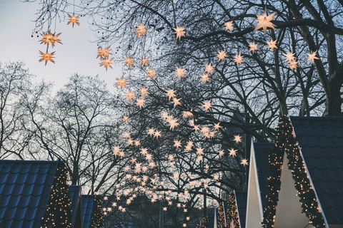Decoration of paper stars on trees over roofs of the Christmas Market during dusk stock photo