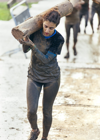 Teilnehmer eines extremen Hindernisrennens trägt einen Baumstamm, lizenzfreies Stockfoto