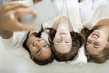 Drei glückliche Teenager-Mädchen liegen auf dem Bett und machen ein Selfie - OJF000094
