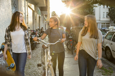 Drei Teenager-Mädchen auf dem Bürgersteig mit Fahrrad und Skateboard - OJF000107
