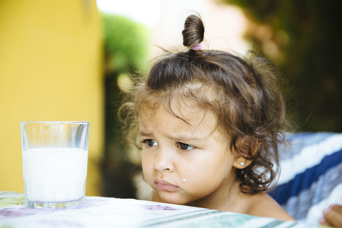 Portrait of unhappy little girl with glass of milk stock photo