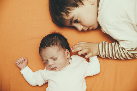 Neugeborenes Mädchen und Bruder auf dem Bett liegend, lizenzfreies Stockfoto