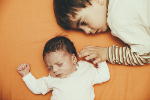 Newborn baby girl and brother lying on bed stock photo