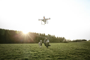 Mann auf einer Wiese fliegt Drohne während sein Hund zuschaut - REAF000023