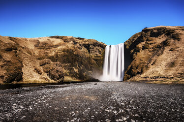 Island, Kleiner Mann in der Landschaft vor dem Skogafoos-Wasserfall stehend - SMAF000424
