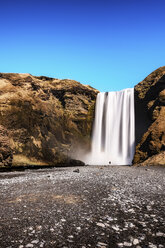 Island, Kleiner Mann in der Landschaft vor dem Skogafoos-Wasserfall stehend - SMAF000425
