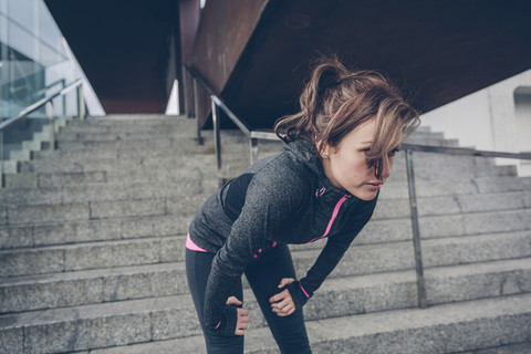 Müde Frau ruht sich nach dem Laufen vor einer Treppe aus, lizenzfreies Stockfoto