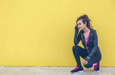 Frau in Sportkleidung hockt vor einer gelben Wand - DAPF000030