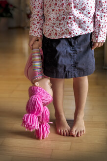 Tiefschnitt eines Mädchens, das auf einem Holzboden steht und eine Puppe hält - EJWF000767