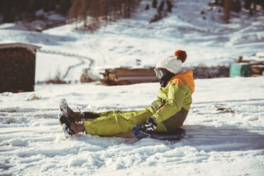 Italien, Vinschgau, Slingia, Junge fährt mit dem Schlitten einen verschneiten Hügel hinunter - MFF002708