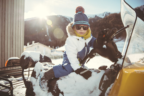 Italien, Vinschgau, Slingia, Junge mit Sonnenbrille auf einem Schneemobil sitzend, lizenzfreies Stockfoto