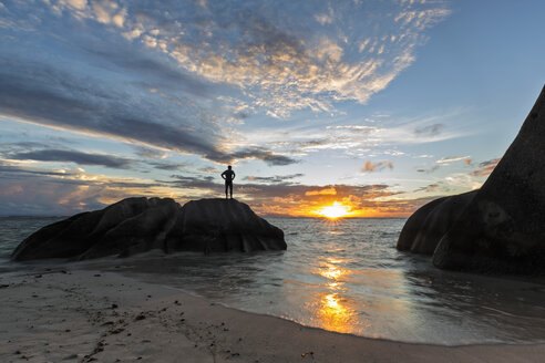 Seychellen, La Digue, Strand, Mann steht auf Granitfelsen bei Sonnenuntergang - FOF008427