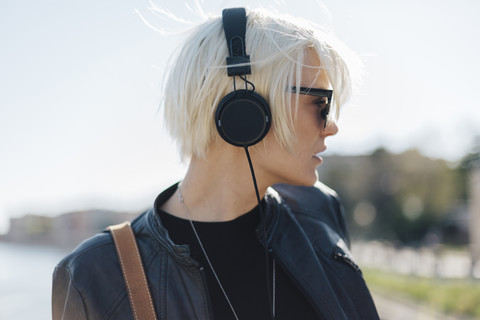 Profil einer blonden Frau mit Sonnenbrille, die mit Kopfhörern Musik hört, lizenzfreies Stockfoto