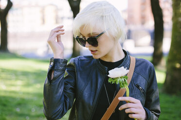 Kühle blonde Frau mit Sonnenbrille hält eine Blume - GIOF000733