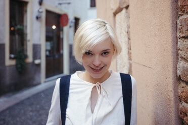 Italy, Verona, portrait of smiling blond woman standing in a narrow alley - GIOF000739