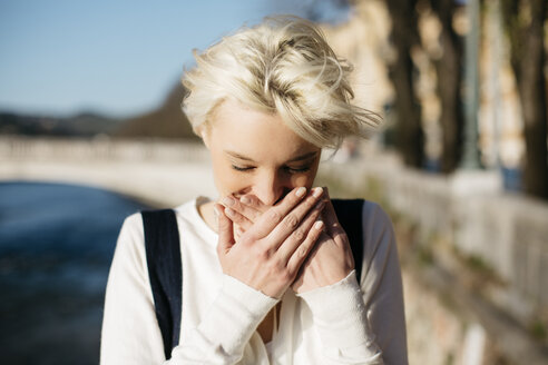 Italien, Verona, blonde Frau, die den Mund mit den Händen bedeckt - GIOF000747