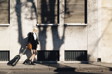 Blonde Frau mit Gepäck auf einem Bürgersteig - GIOF000752