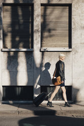 Blond woman with luggage walking on a pavement - GIOF000753