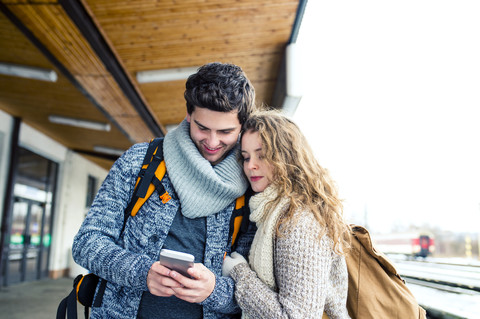 Junges Paar auf dem Bahnsteig, das auf sein Handy schaut, lizenzfreies Stockfoto