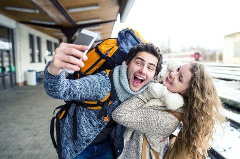 Playful young couple on station platform taking a selfie - HAPF000206