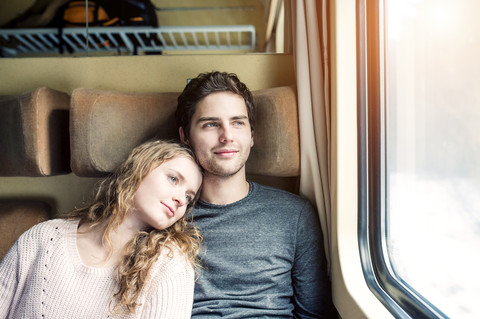 Lächelndes junges Paar im Zugwaggon schaut aus dem Fenster, lizenzfreies Stockfoto