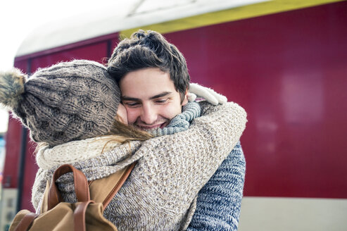 Glückliches junges Paar, das sich vor einem Zug umarmt - HAPF000215
