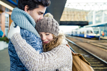 Lächelndes junges Paar, das sich auf dem Bahnsteig umarmt - HAPF000216
