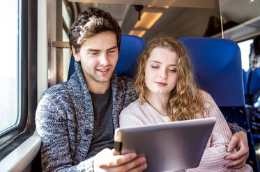 Smiling young couple in train car using digital tablet - HAPF000226