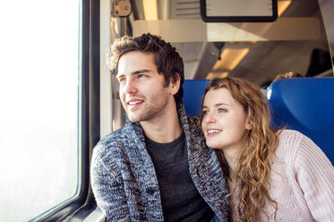 Lächelndes junges Paar im Zugwaggon schaut aus dem Fenster - HAPF000227