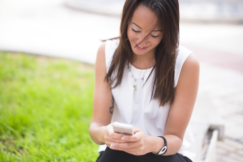 Junge Frau im Freien schaut auf ihr Handy, lizenzfreies Stockfoto