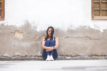 Junge Frau sitzt im Freien an einer Mauer - SIPF000173