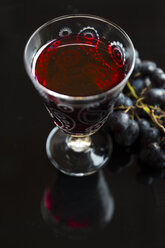 Glass of red wine and blue grapes on black ground - SARF002544