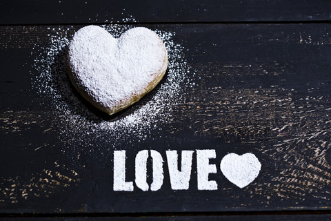 The word 'Love' stenciled with icing sugar and a heart-shaped cruller on dark wood stock photo