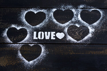Hearts and the word 'Love' stenciled with icing sugar on dark wood - MAEF011283
