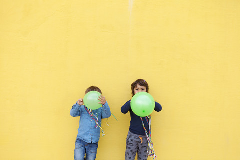 Two little boys with green balloons and streamers standing in front of yellow wall stock photo